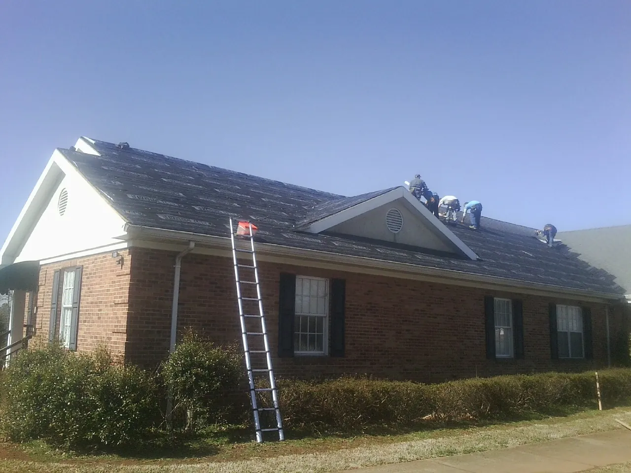 Crew tearing shingles off a brick ranch roof with a ladder set — Metal Roof Repair work by our crew in Rush City
