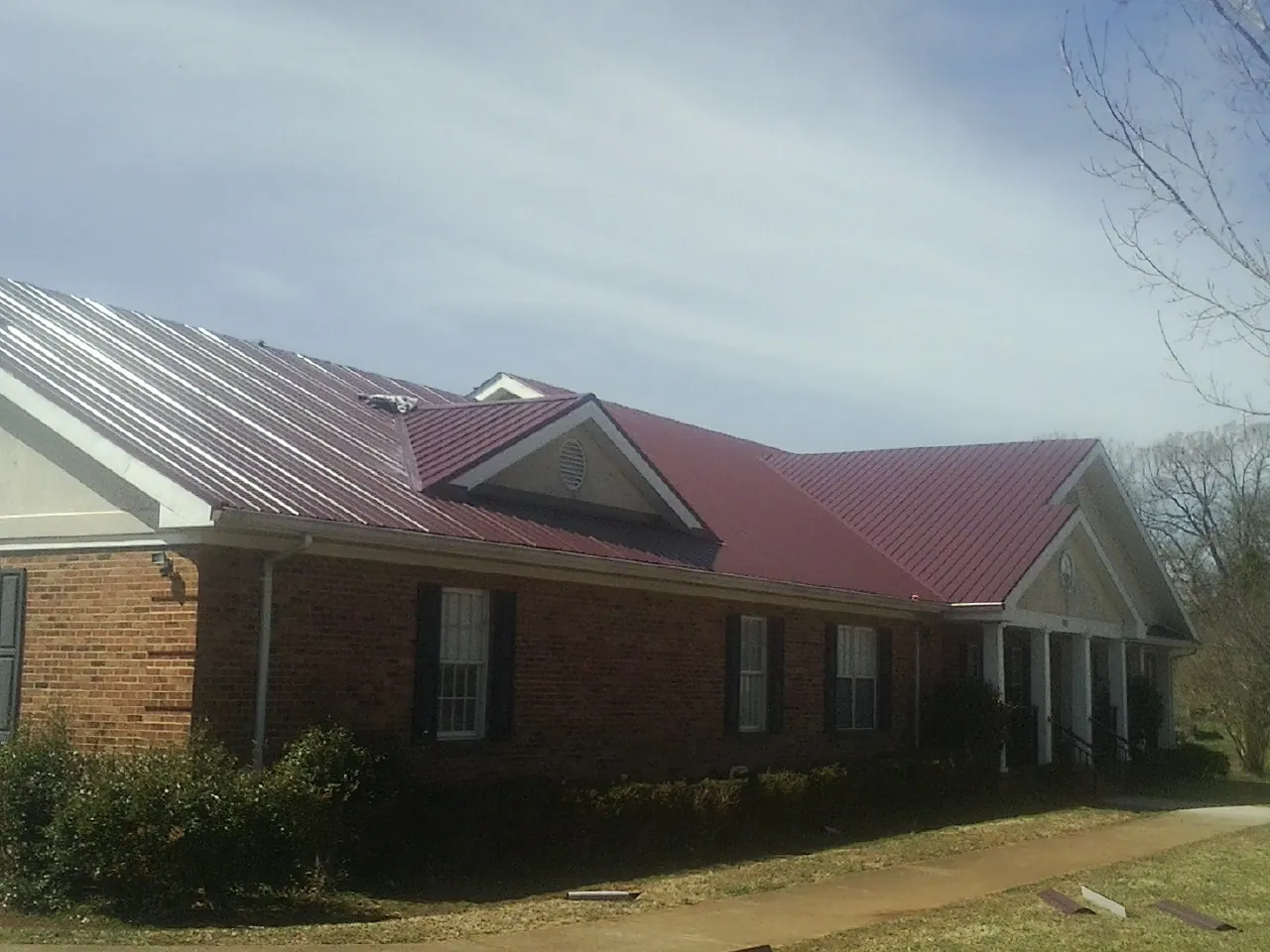 Red metal roof with gabled entries on a long brick building, from a Hail Damage Roof Repair job in Rush City