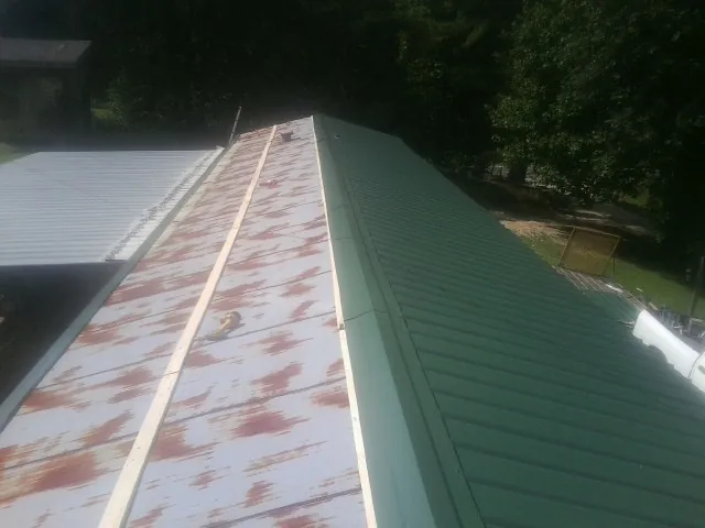 Old rusted panels beside newly installed green metal roofing — Wind Damage Roof Repair by Roofing Brothers in Rush City