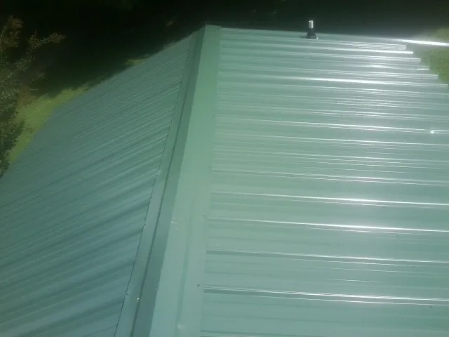 New green metal panels meeting at the ridge of a roof — Flat Roof Repair work by our crew in Rush City