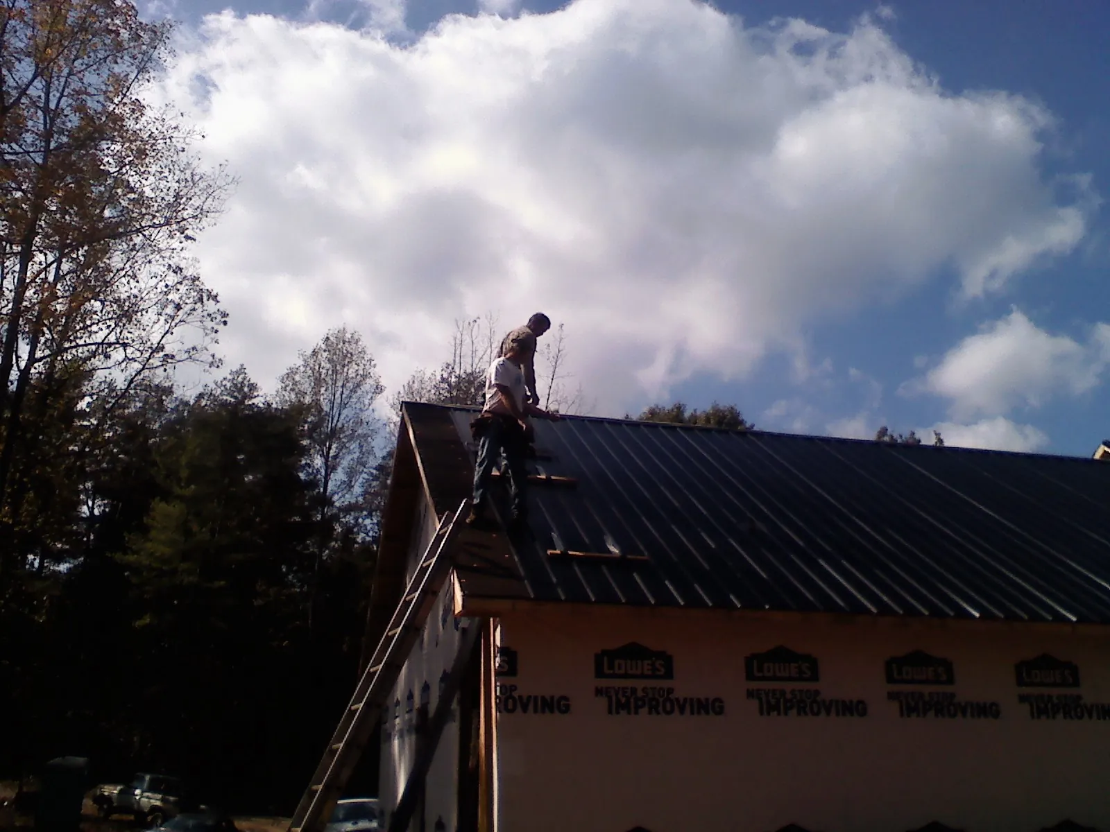 Roofer fastening dark metal panels high against a cloudy sky, from a Roof Inspection job in Rush City