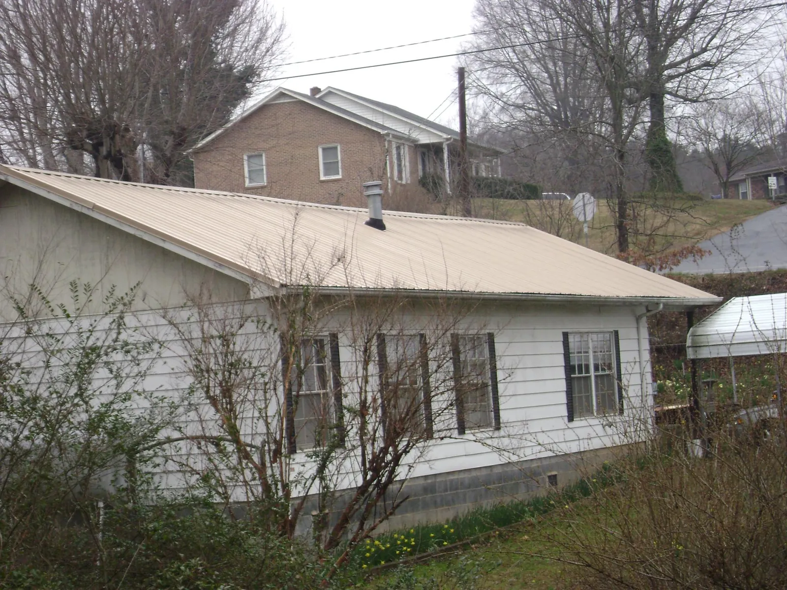 Tan metal roof on a white sided house set into a hillside — Commercial Roofing by Roofing Brothers in Rush City